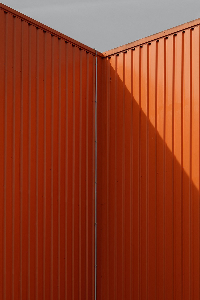 Blick auf die Ecke einer orangefarbenen Lagerhalle aus Wellblech.