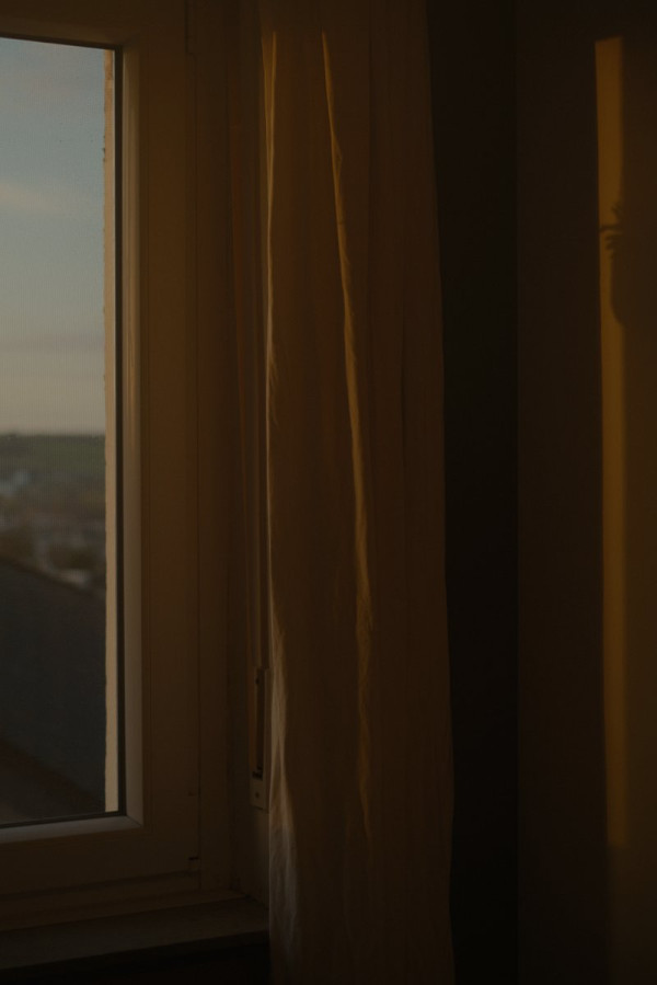 Durch ein Fenster fällt Licht der Abendsonne auf einen neben dem Fenster hängenden Vorhang und eine Schrankwand. Das Licht ist tief orange und färbt die Szene in warme Orange-Töne.