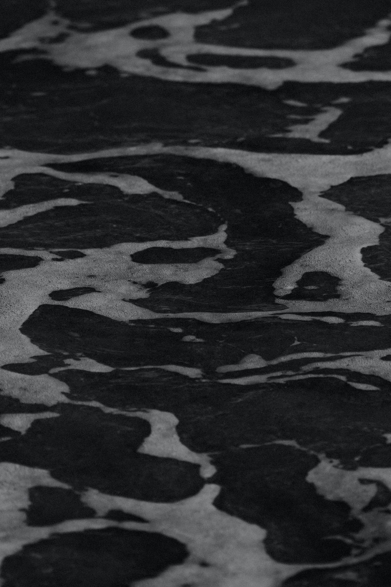 Schwarz-Weiß Fotografie. Nahaufnahme von weißer Gischt auf dunklem Wasser.